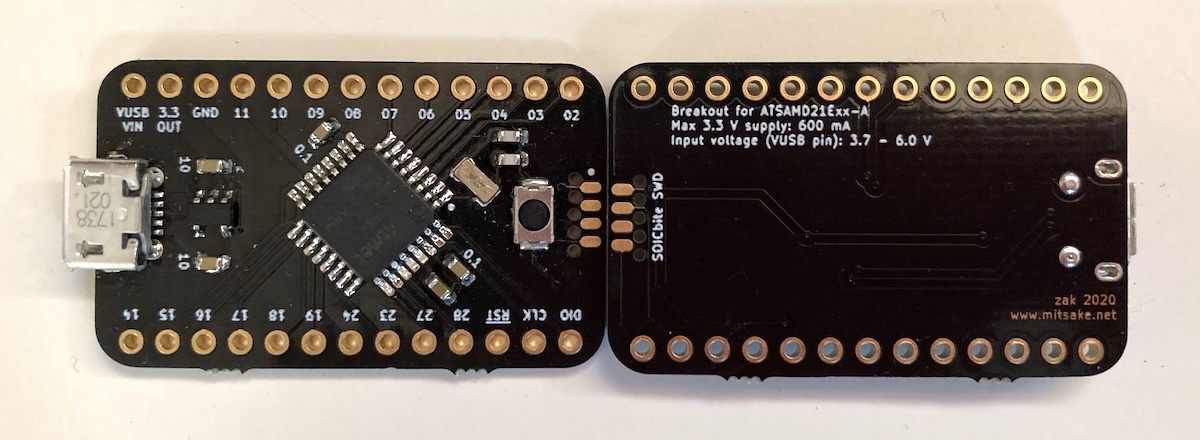 Two circuit boards lying side by side. The left-hand board is face up, showing two rows of through-hole pads and some components such as ICs and capacitors. The right-hand board is face-down with silkscreen text reading 'Breakout for ATSAMD21Exx-A / Max 3.3 V supply: 600 mA / Input voltage (VUSB pin): 3.7 - 6.0 V'