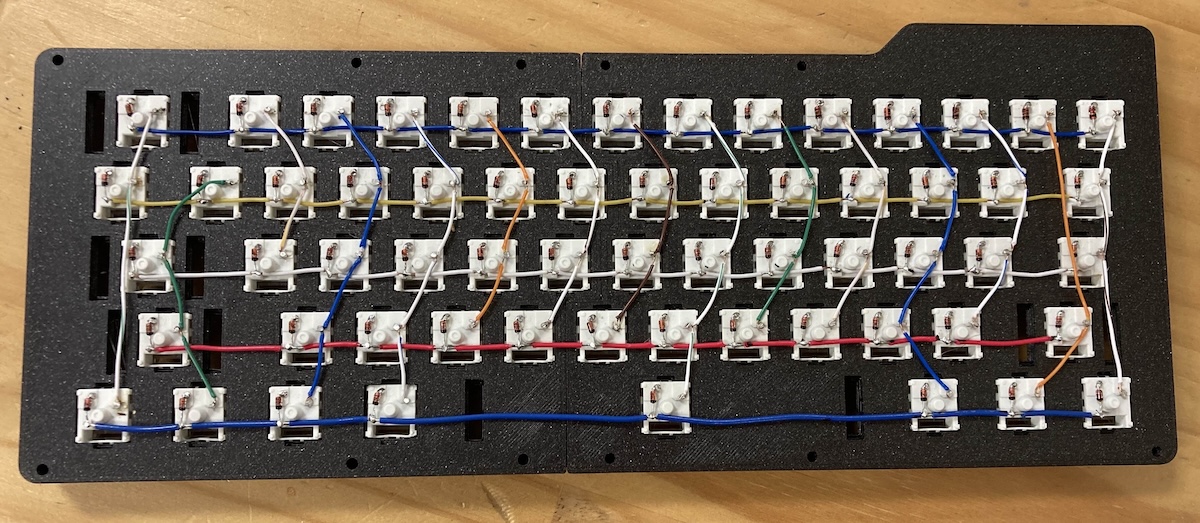 The underside of a keyboard. The columns and rows of wires that connect the keyswitches are visible, as are the diodes